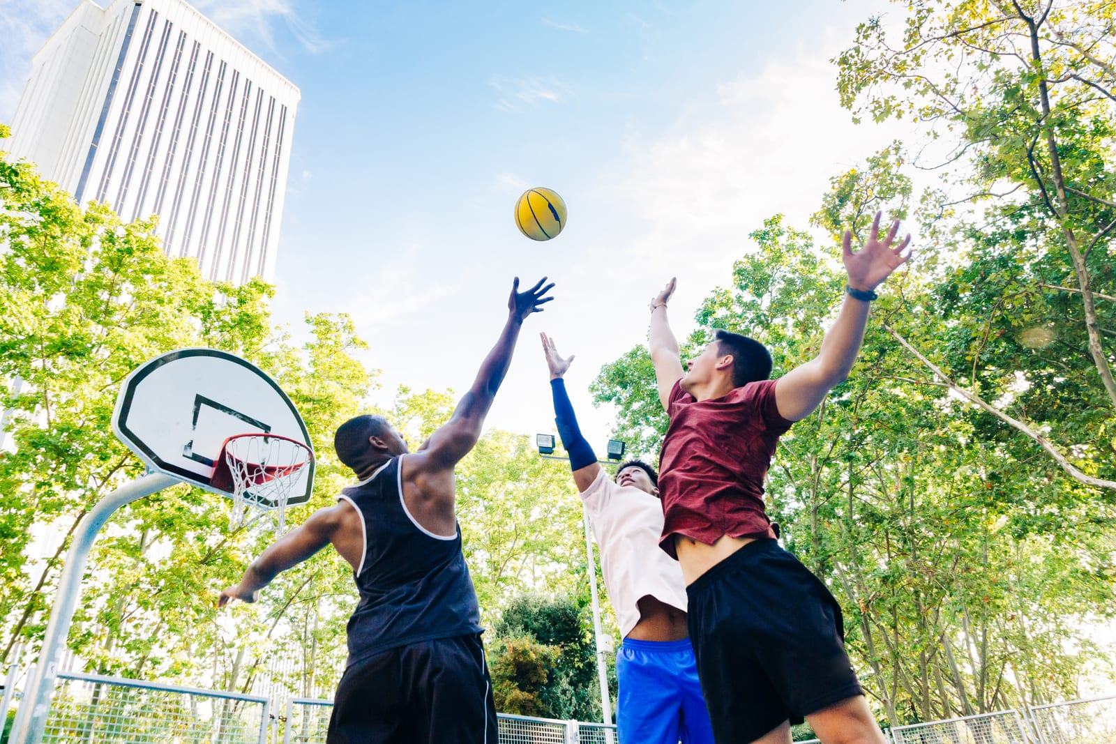 Three players going up for a rebound in a pickup basketball game outdoors