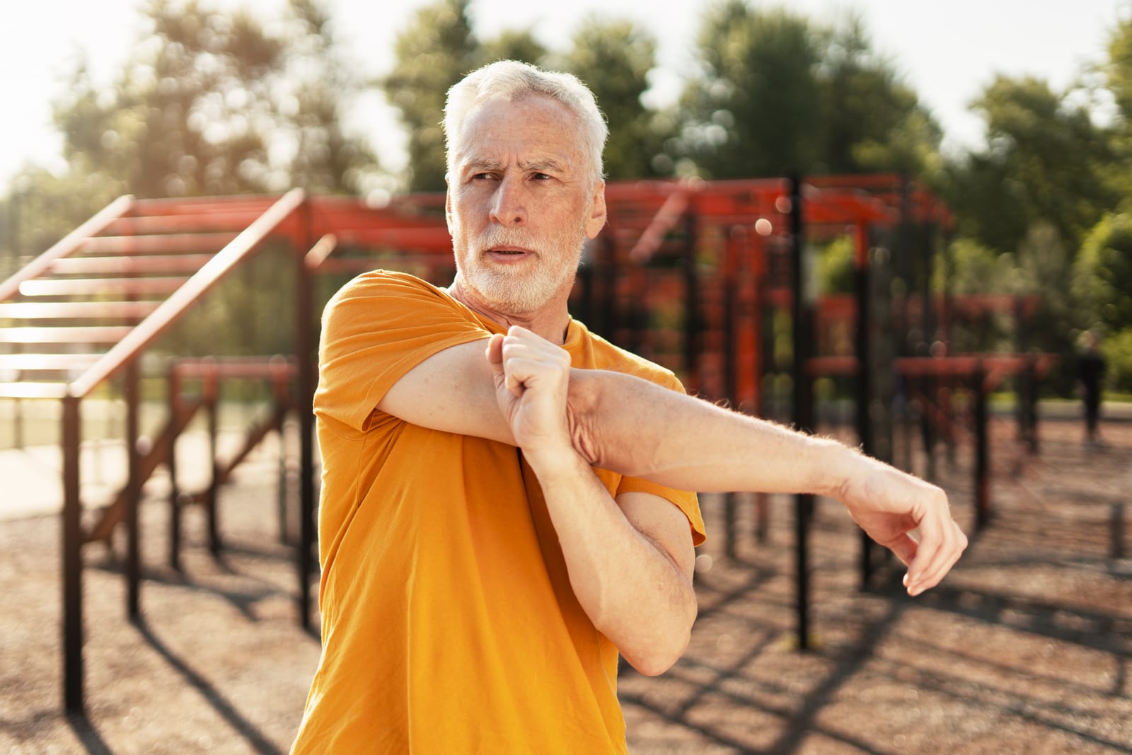 Older man doing a cross-body shoulder stretch, the kind of home exercise that comes out of a visit