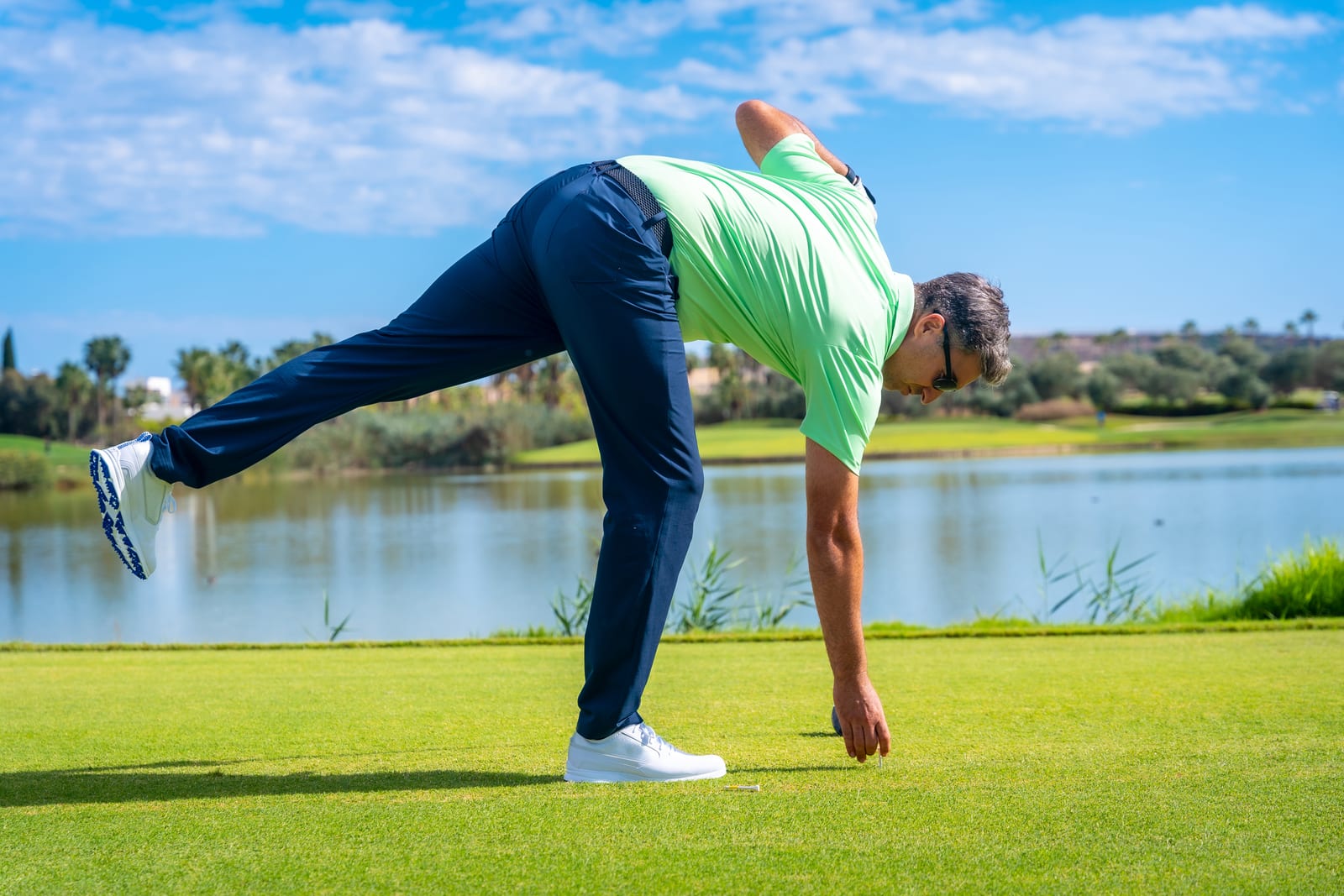 Golfer hinging at the hip with the back leg extended to reach the tee, a pattern that needs a stable base