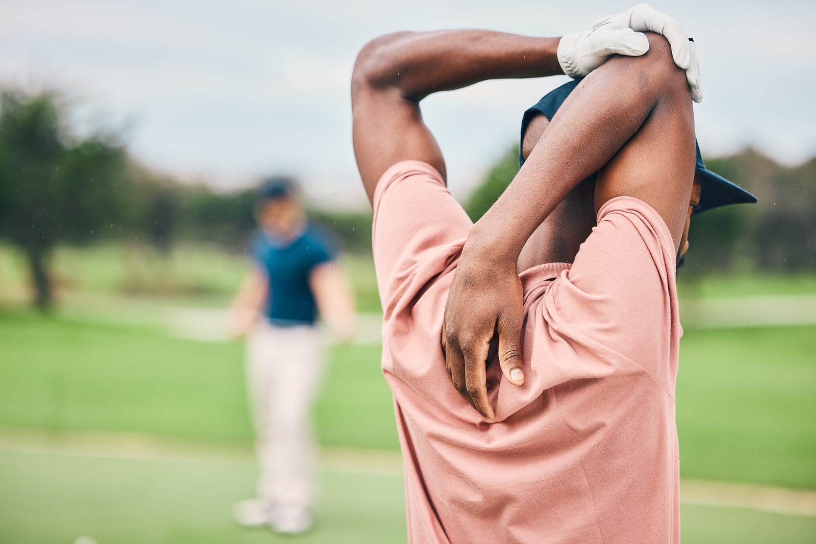 Golfer stretching the shoulder and upper arm out on the course, keeping the joint loose for the swing