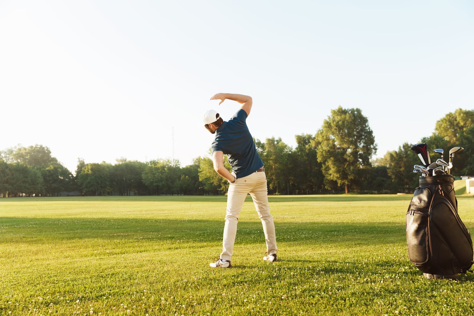 Golfer working through a standing side bend beside his bag before a round