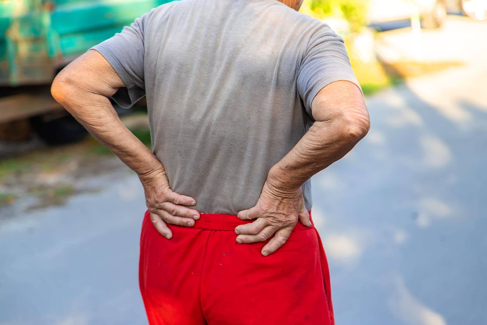 Person standing outdoors with both hands pressed to the lower back, where sciatica symptoms typically begin
