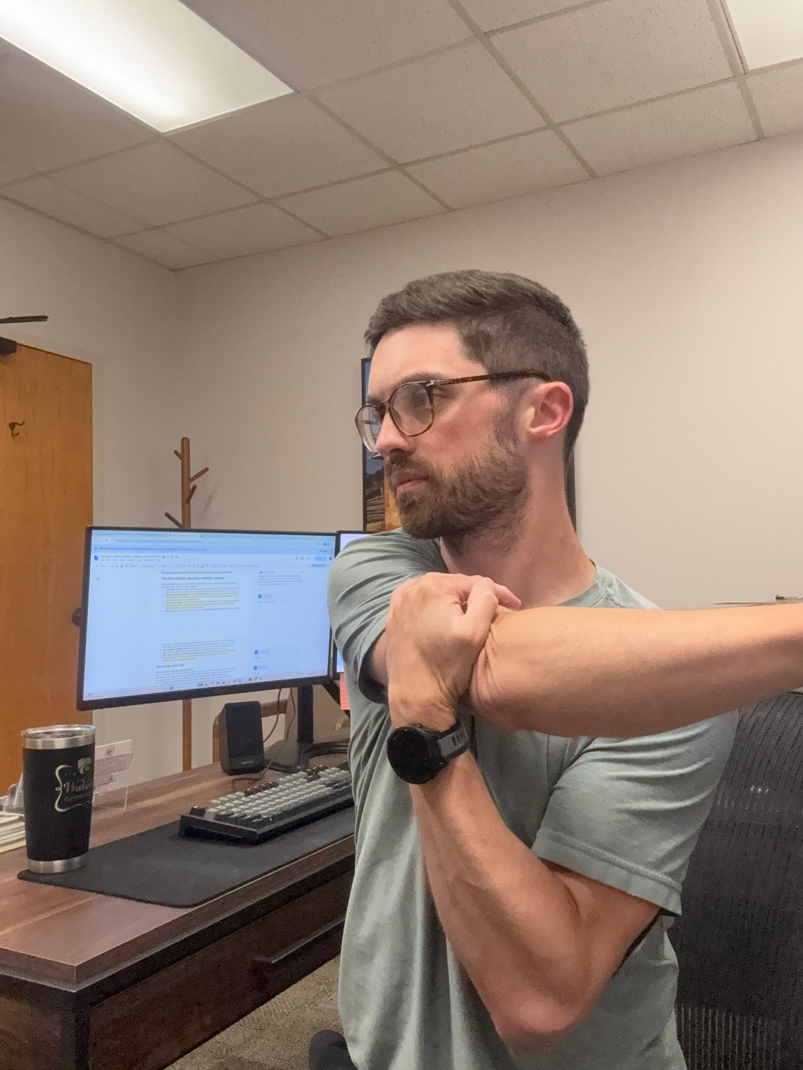 Cross-body shoulder stretch done at a desk to release the back of the shoulder