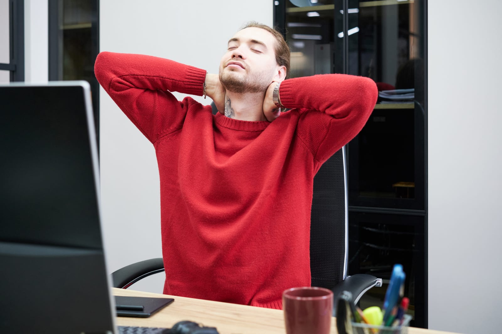Office worker leaning back from the screen with hands behind the head, taking a break from a held posture