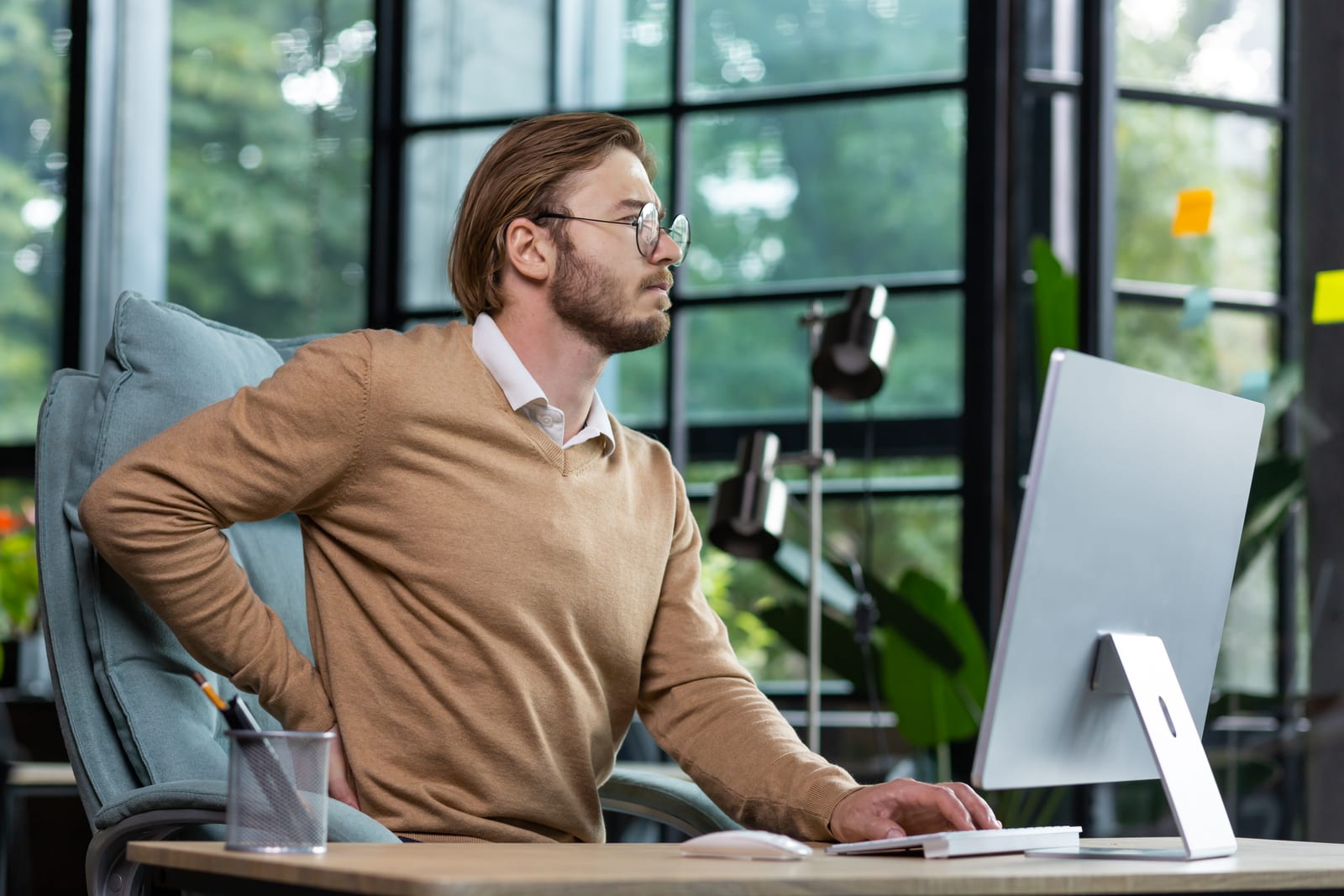 Office worker at a desk reaching for his sore lower back, a common everyday cause of low back pain